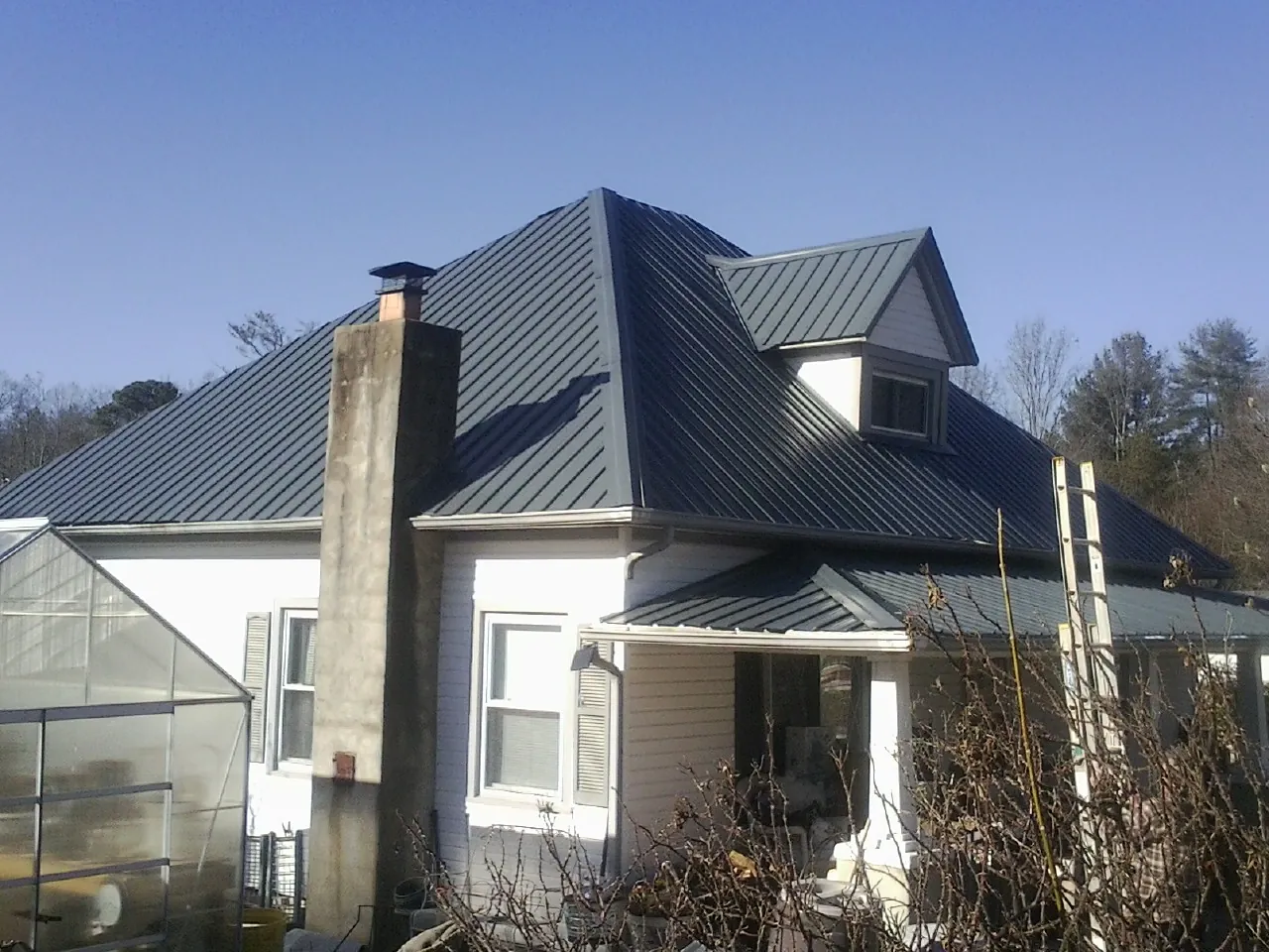 Dark blue standing seam metal roof on a white farmhouse with dormer — Slate & Tile Roof Repair by Roofing Brothers in Suttons Bay