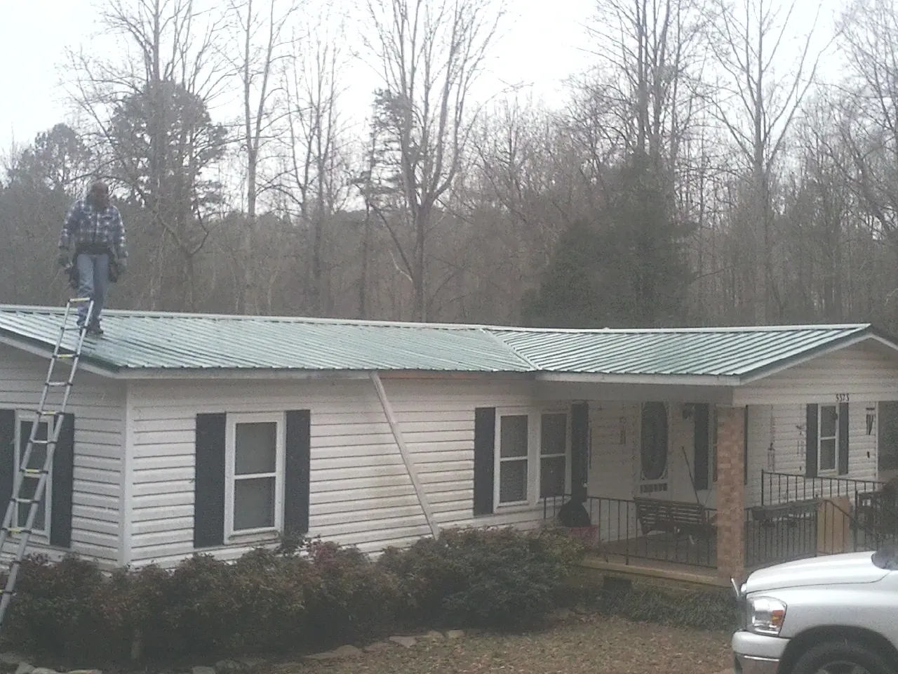Worker on a ladder beside a new green metal roof on a ranch home in Suttons Bay