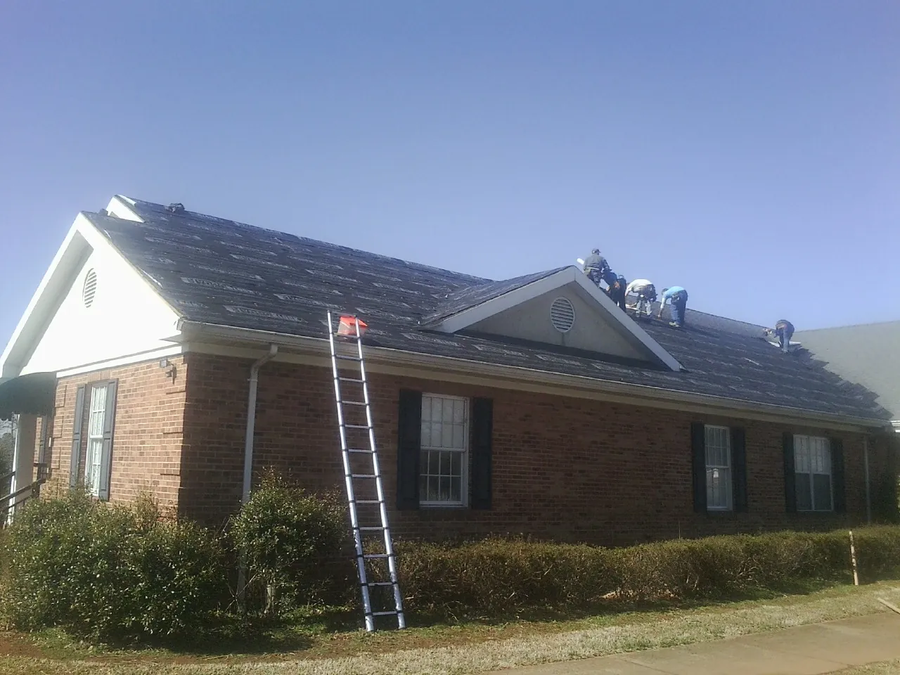 Crew tearing shingles off a brick ranch roof with a ladder set — Metal Roof Repair work by our crew in Suttons Bay