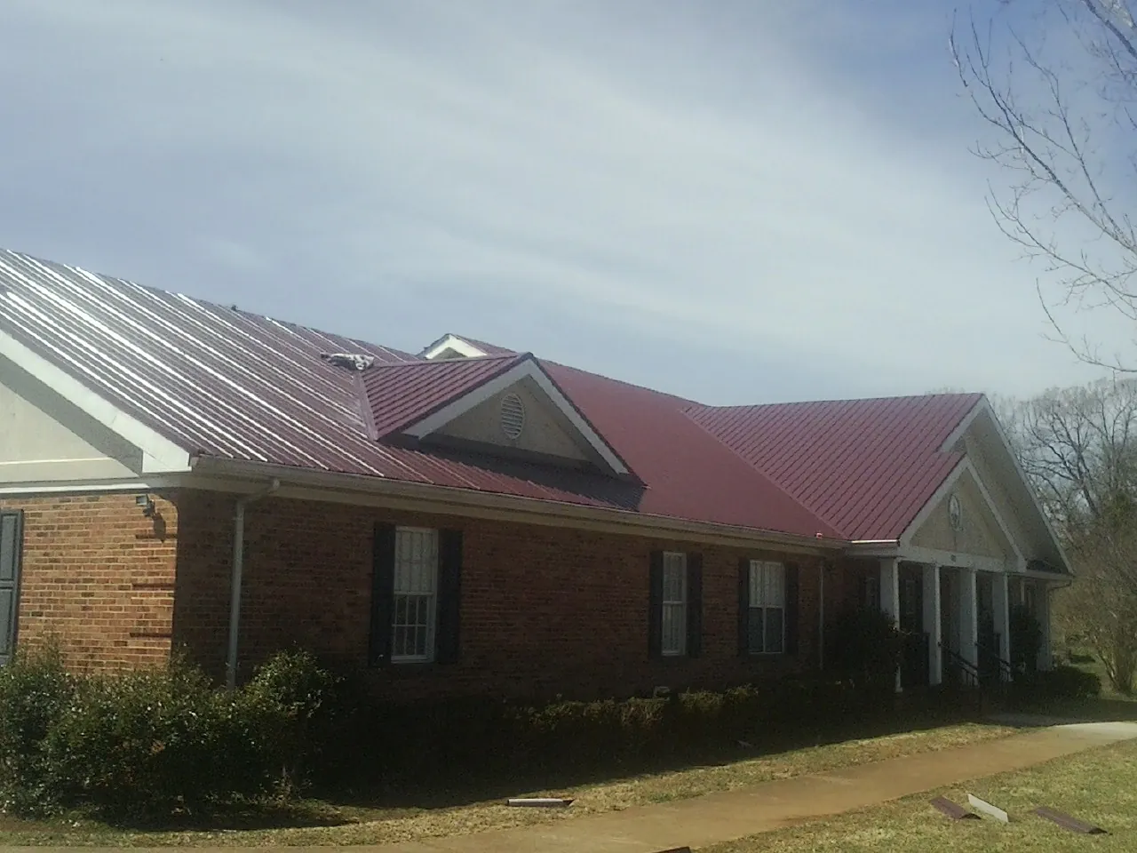 Red metal roof with gabled entries on a long brick building, from a Hail Damage Roof Repair job in Suttons Bay