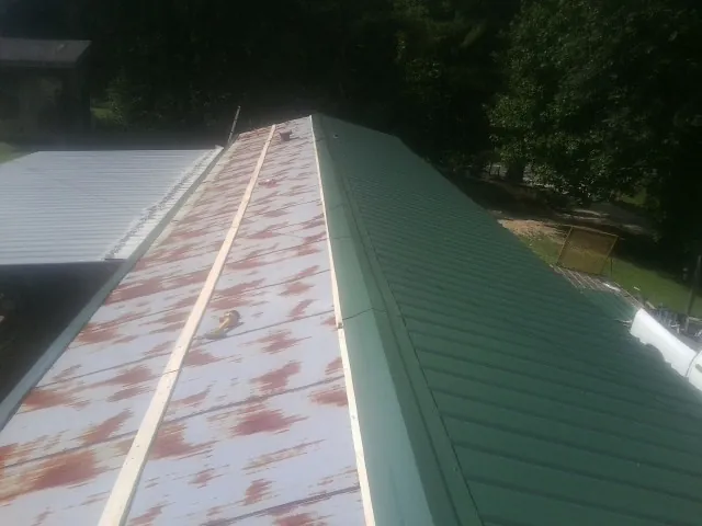 Old rusted panels beside newly installed green metal roofing — Wind Damage Roof Repair by Roofing Brothers in Suttons Bay