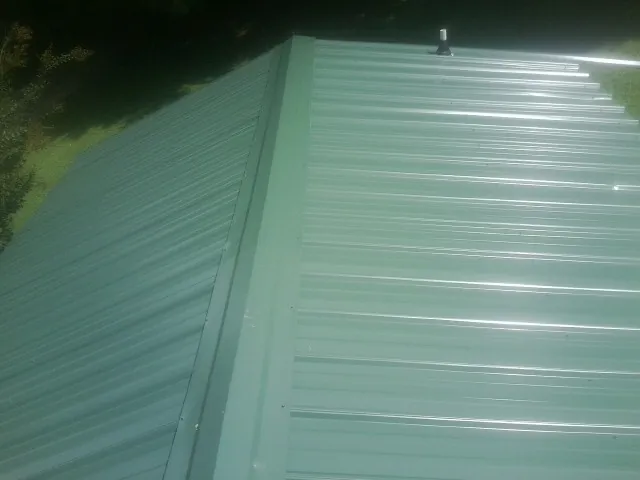 New green metal panels meeting at the ridge of a roof — Flat Roof Repair work by our crew in Suttons Bay