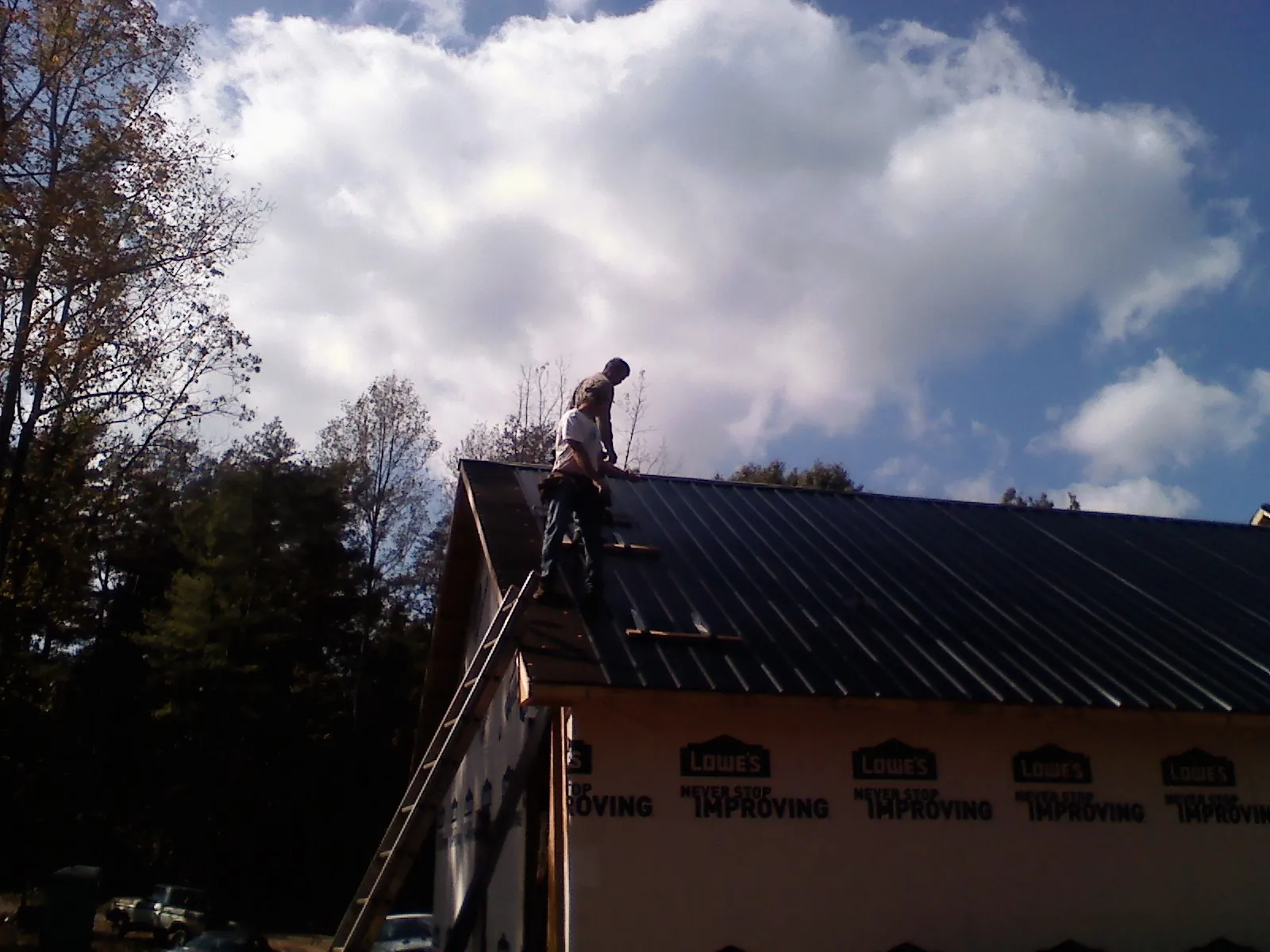 Roofer fastening dark metal panels high against a cloudy sky, from a Roof Inspection job in Suttons Bay
