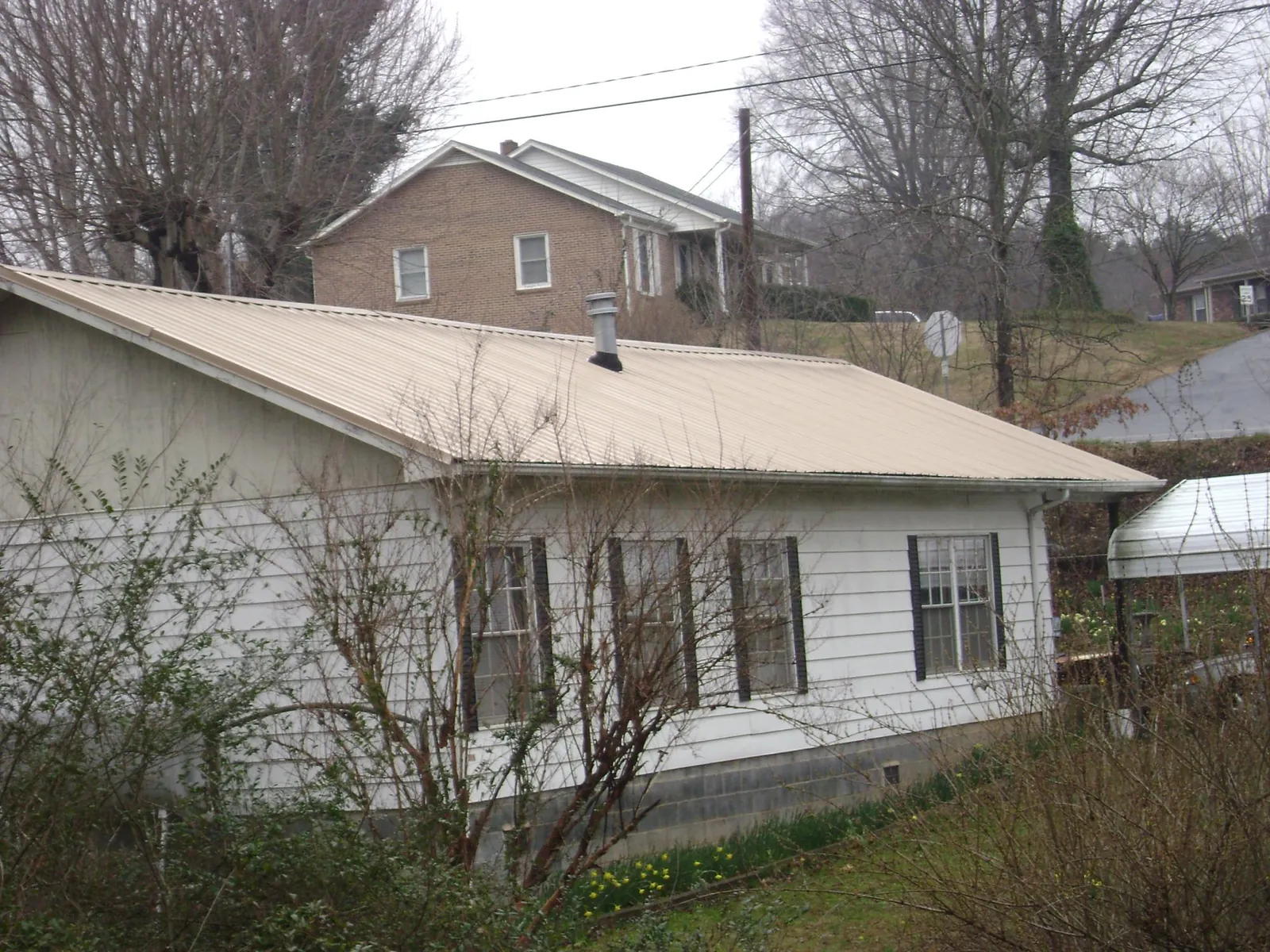 Tan metal roof on a white sided house set into a hillside — Commercial Roofing by Roofing Brothers in Suttons Bay