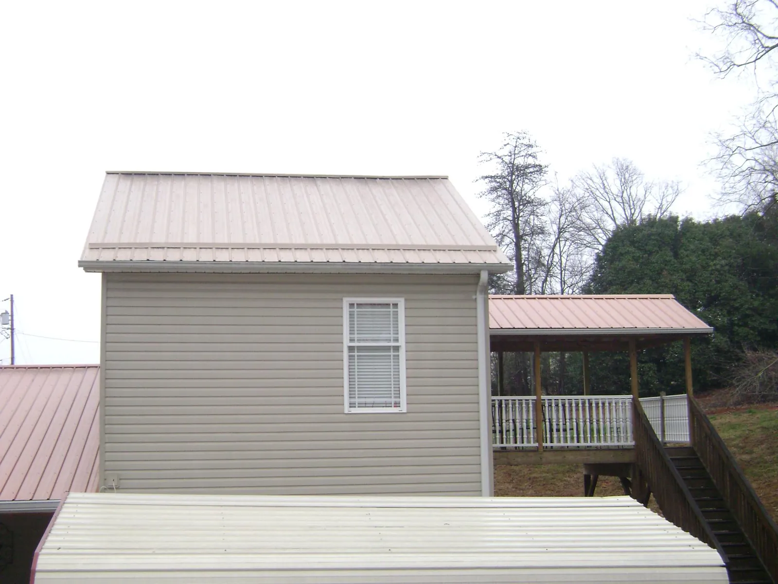 Tan metal roofs on a two story addition and attached porch, from a Roof Replacement job in Suttons Bay